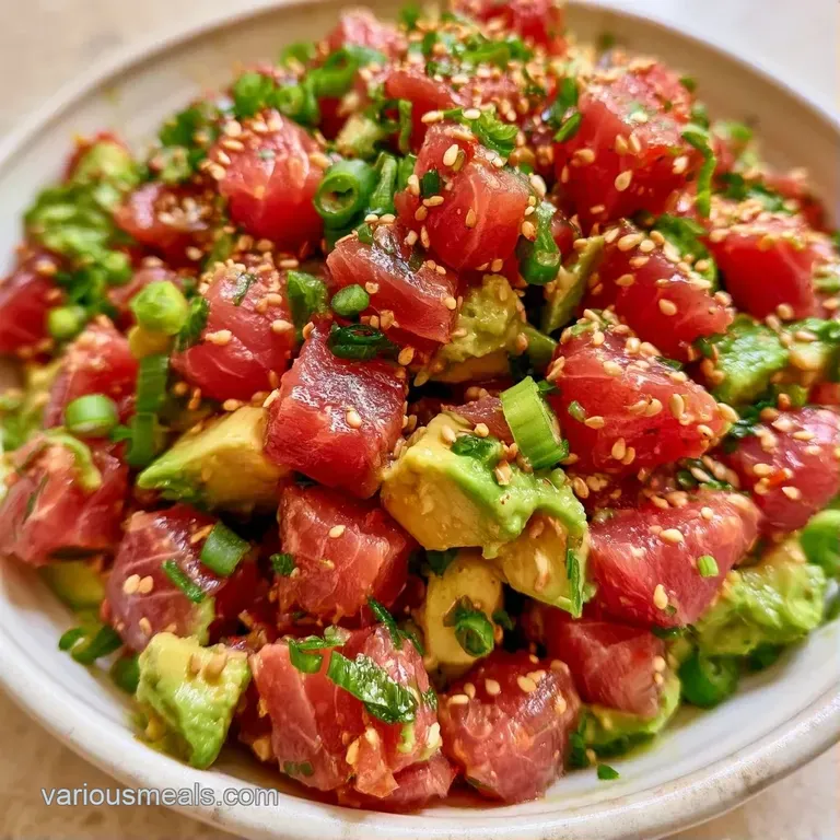 Two elegant bowls of cubed ruby red fish and pale green avocado, topped with sesame seeds on a light wood surface.
