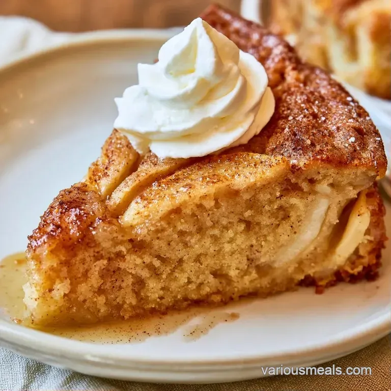 Golden-brown cake slice on a white ceramic plate, garnished with a swirl of cream and tart red apple slices.