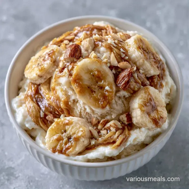 Two smooth scoops of pale yellow frozen treat in a crystal bowl with fresh mint leaves and crushed almonds.