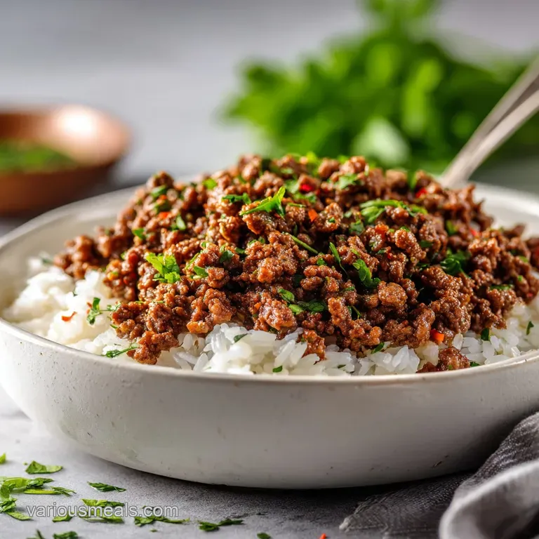 Savory ground beef seasoned with herbs piled high, artfully arranged on a white plate with a sprig of fresh garnish.