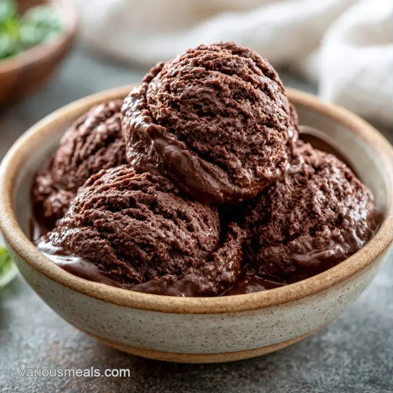 Three smooth scoops of dark chocolate ice cream on white porcelain accented with tart raspberries and gold flakes.
