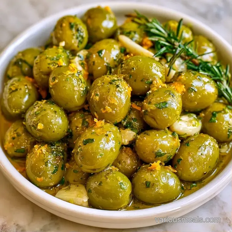 Assorted green and black olives in a glass dish, shimmering with oil and garnished with thin citrus wheels.