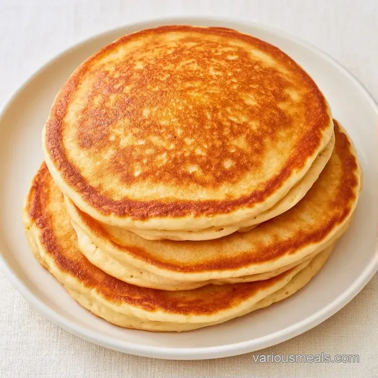Golden circles of thick, fluffy cakes stacked neatly on a white ceramic plate against a soft morning light background.