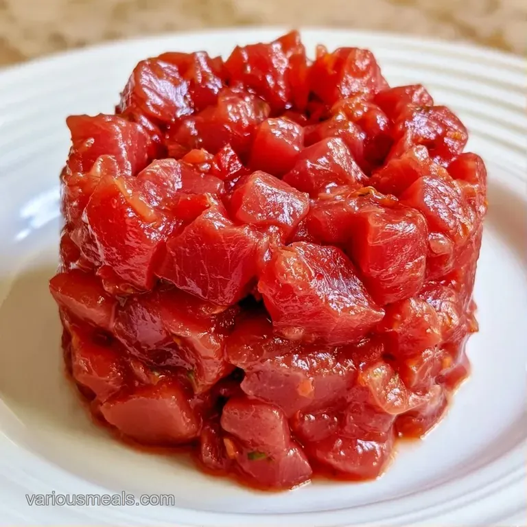 A precise tower of ruby-red diced fish topped with micro-cilantro and a glossy glaze on a modern slate platter.