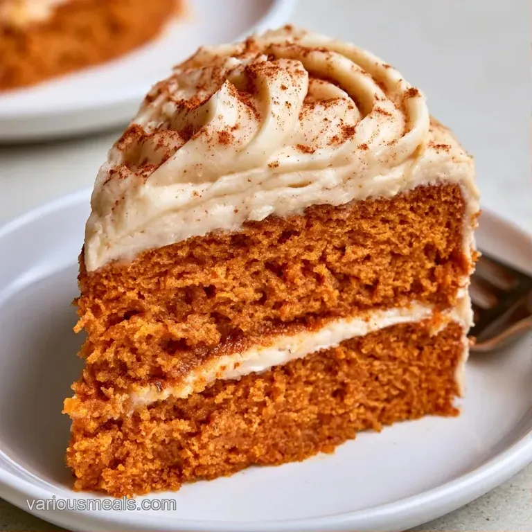 A neat slice of spiced orange cake with thick swirls of frosting served on a white ceramic plate with a silver fork.