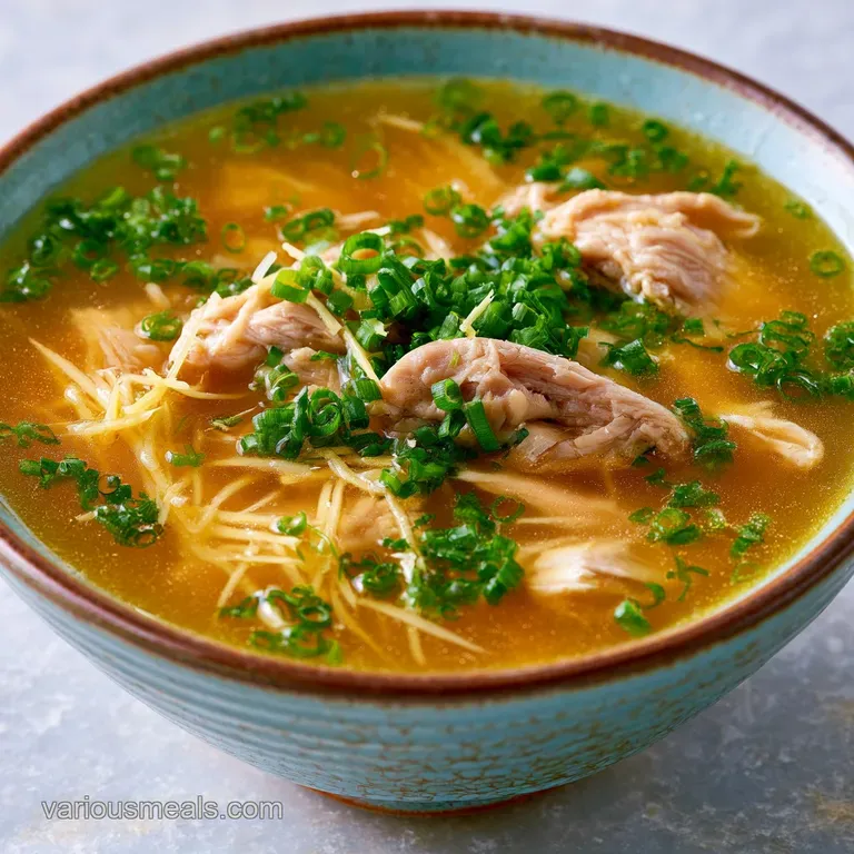 Steaming white ceramic bowl of clear gold soup garnished with bright green scallions on a rustic wooden surface.