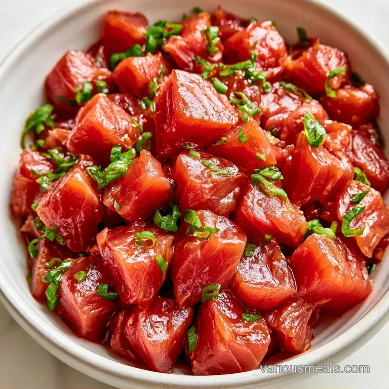 Vibrant red tuna cubes and sliced cucumber in a dark bowl, topped with chopped scallions and white sesame seeds.
