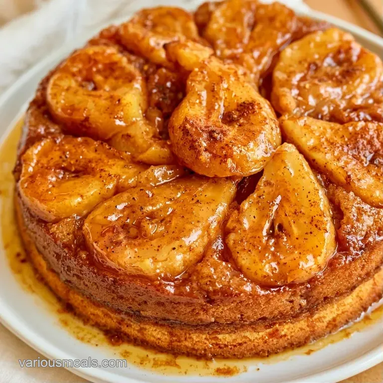 A single slice of golden sponge cake on a white plate, crowned with a glazed pear slice and cinnamon dust.
