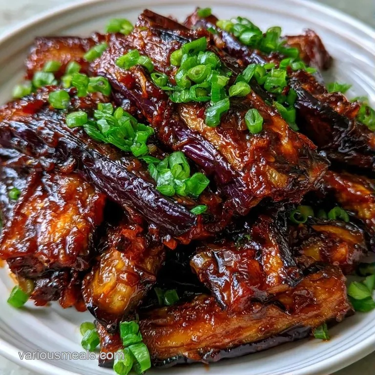 Tender, glazed purple eggplant strips topped with toasted sesame seeds and sliced green onions on a slate plate.