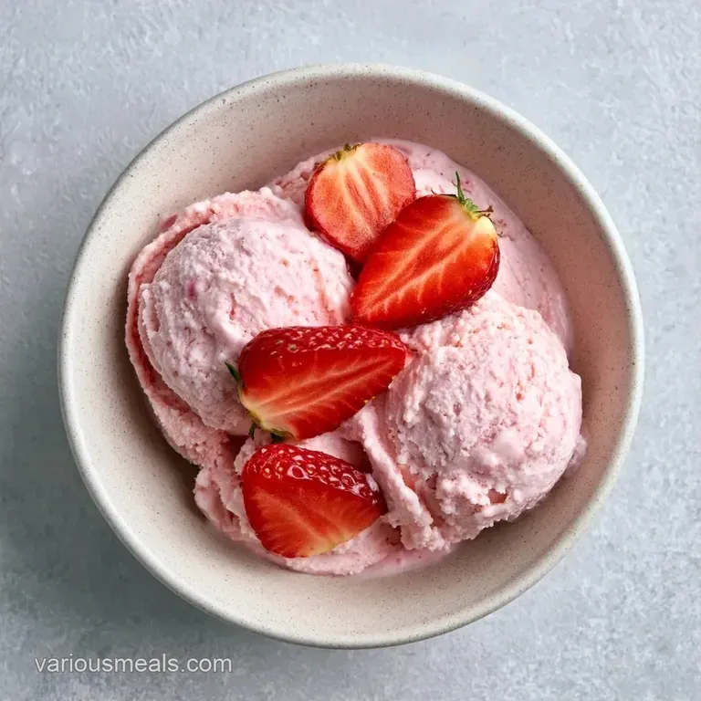 Two smooth pink scoops of frozen dessert in a white ceramic bowl, garnished with a mint leaf and fresh strawberry.
